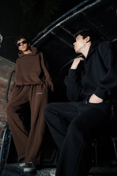 Two individuals wearing brown and black tracksuits in a dark setting.